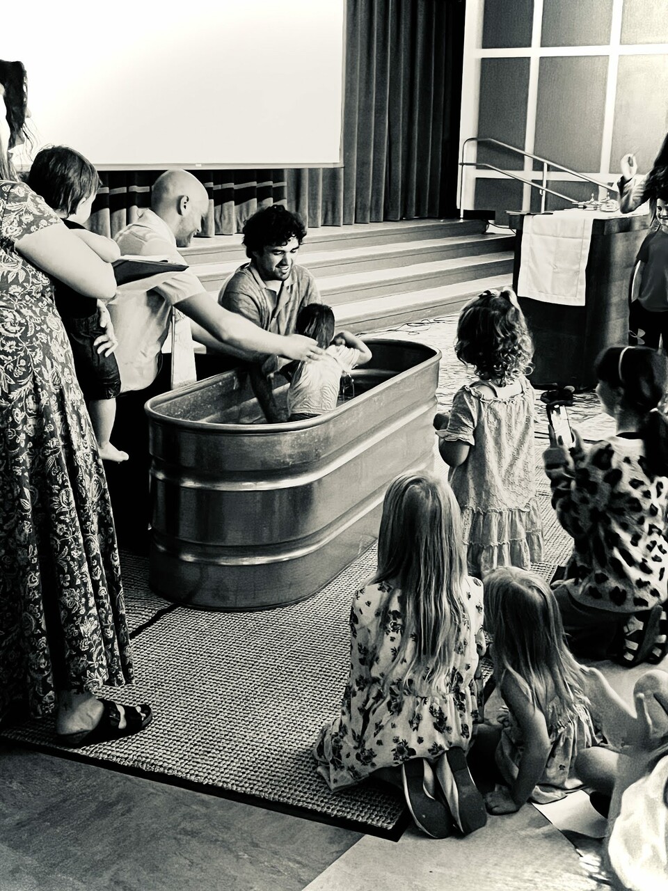 Fr. Lenny baptizes a child at The Table as Church Planting Curate Gabriel Roman assists and the congregation's children look on.
